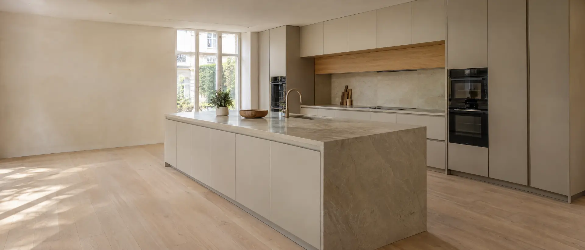 Cuisine moderne beige et bois avec îlot central en pierre naturelle, baignée de lumière par de grandes fenêtres