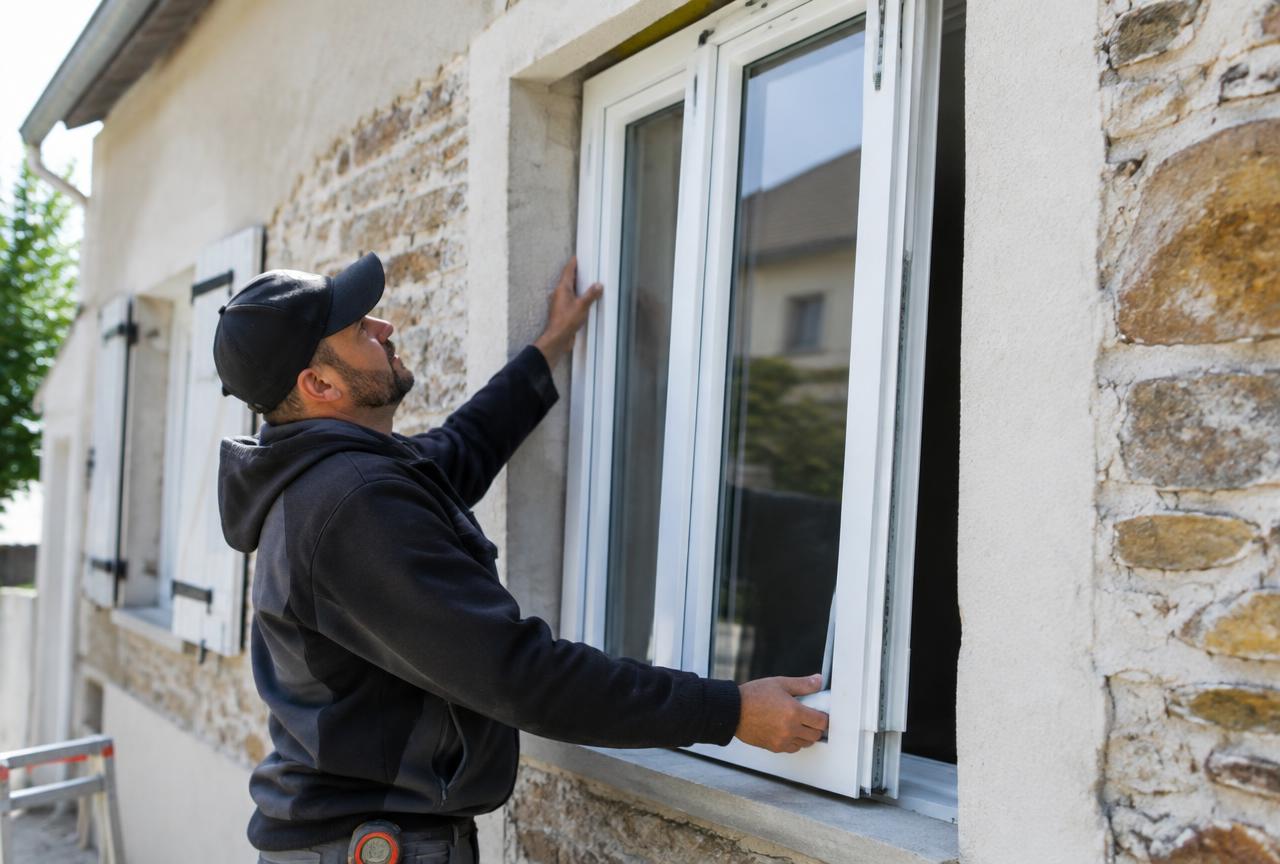 Poseur installant une fenêtre PVC double vitrage sur une maison en pierre